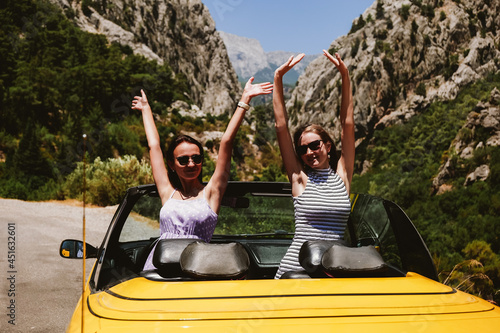 Two young woman in yellow car enjoying vacation