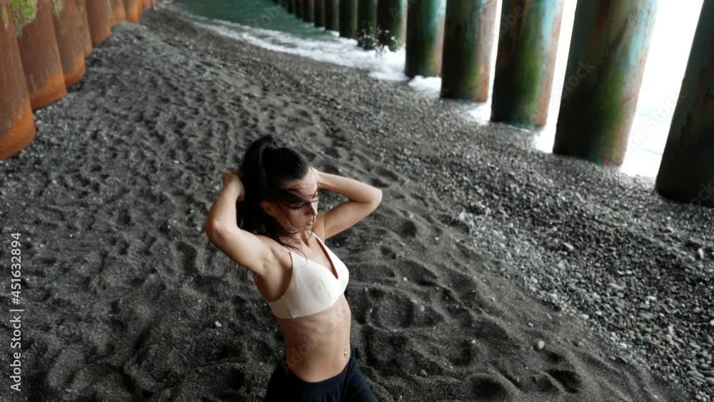 modern dance rehearsal at nature, woman is dancing under sea pier on pebble beach modern dance rehearsal at nature, woman is dancing under sea pier on pebble beach