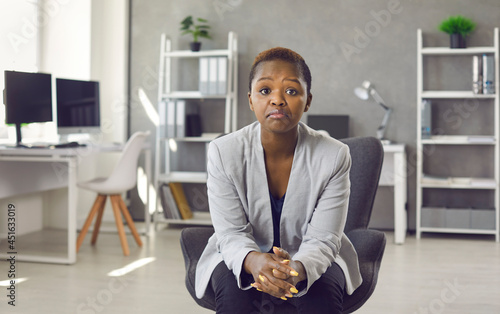 Portrait of black business woman in suit sitting on office chair looking at you with face expression that could be interpreted as both disappointed unimpressed and impressed 'Hmm not bad' expression