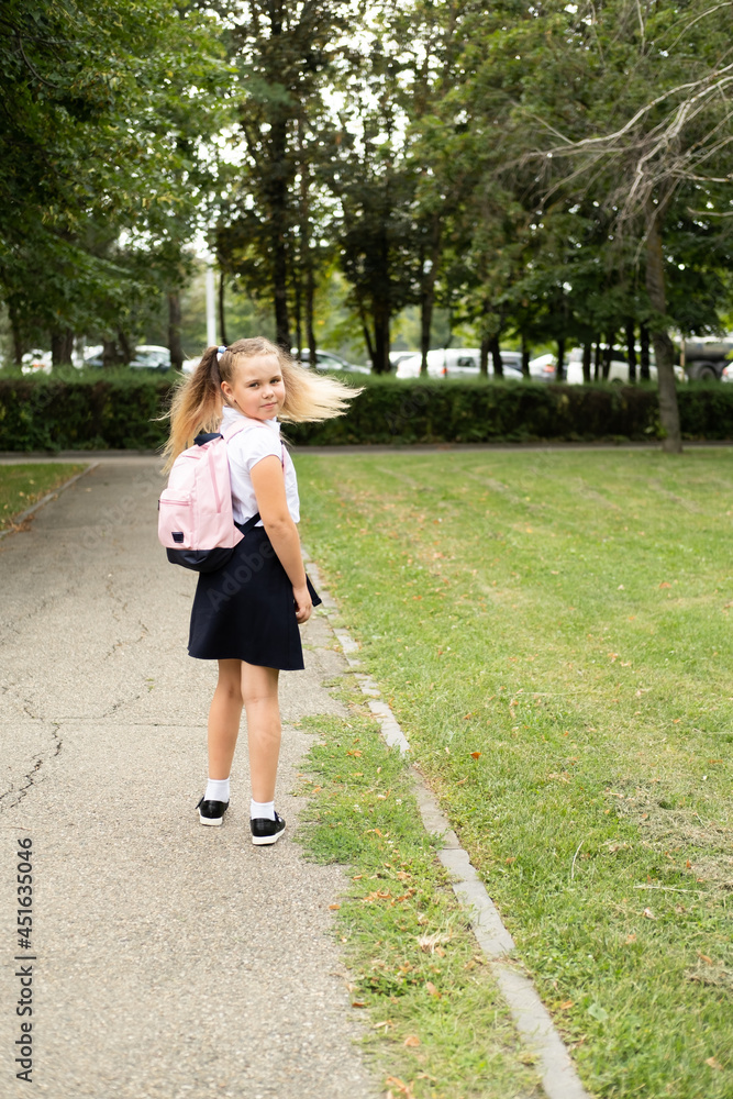 smiling blonde schoolgirl in school uniform with pink backpack going to school outdoor