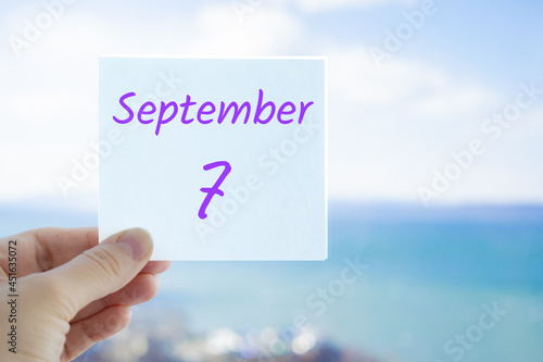 7th September. Hand holding sticker with text September 7 on the blurred background of the sea and sky. Copy space for text. Month in calendar concept