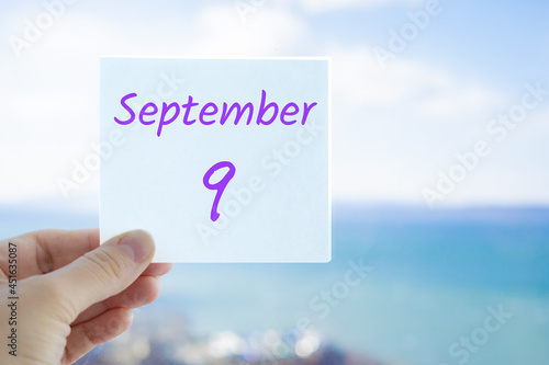 9th September. Hand holding sticker with text September 9 on the blurred background of the sea and sky. Copy space for text. Month in calendar concept