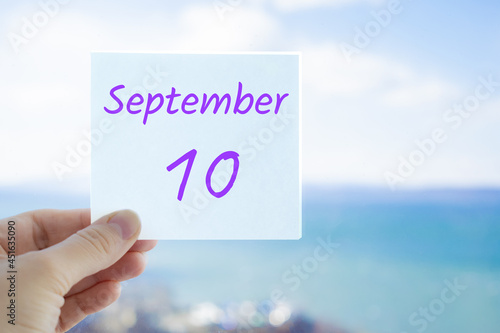 10th September. Hand holding sticker with text September 10 on the blurred background of the sea and sky. Copy space for text. Month in calendar concept