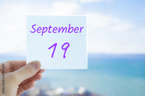19th September. Hand holding sticker with text September 19 on the blurred background of the sea and sky. Copy space for text. Month in calendar concept