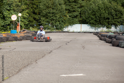 A girl or a woman in a hard hat rides a go-kart on a special track fenced with rubber wheels. Active recreation and sports on transport. Preparation and training for competitions. 