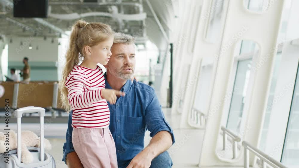 Senior father and his lovely daughter looking at airplanes through the glass window and chatting with pleasure emotions. Travel with baby at the airport concept Senior father and his lovely daughter looking at airplanes through the glass window and chatting with pleasure emotions. Travel with baby at the airport concept