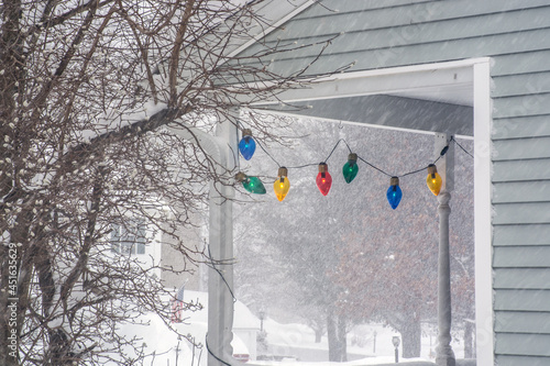 Side of house during winter storm or blizzard. Christmas lights hanging on front porch of snowy house 