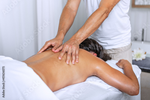 Relaxed young woman lying face down on massage table and enjoying remedial body massage by professional masseur in spa salon