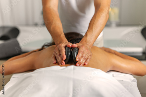 Rear view of a woman receiving a back massage with stones by professional male masseur in health spa