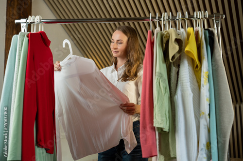 Beautiful thoughtful woman stylist chooses clothes on a hanger in the dressing room