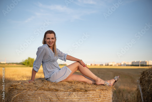 Portrait of a young beautiful blonde girl in a light dress on the field near the straw. © shymar27