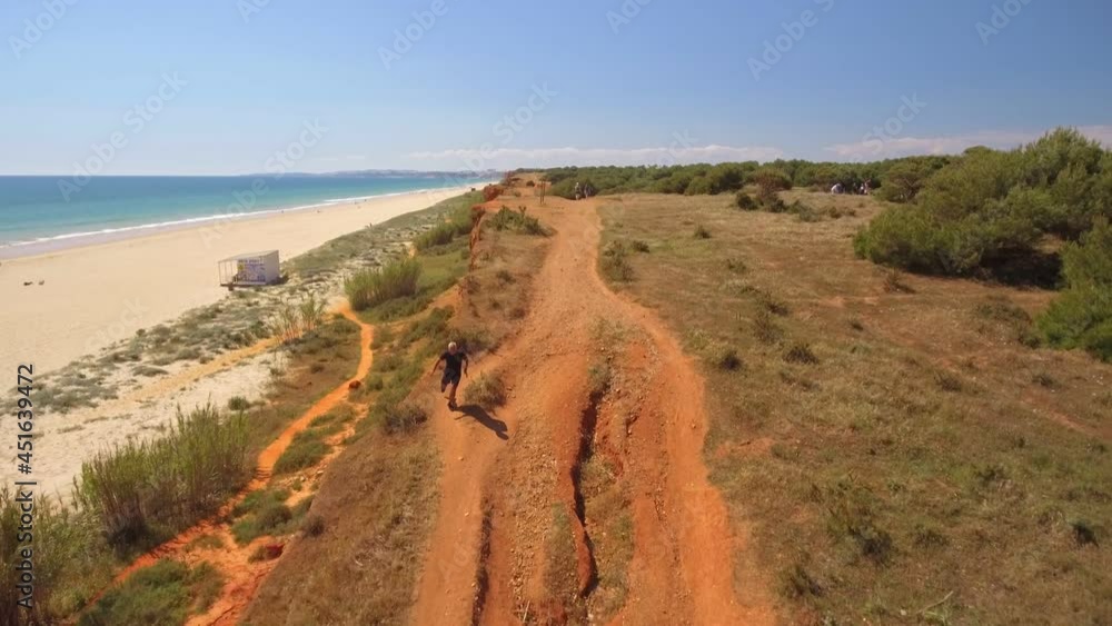Aerial view of an elderly man running along the ocean coast. A cliff steeped in greenery. Sunny day. Front view.