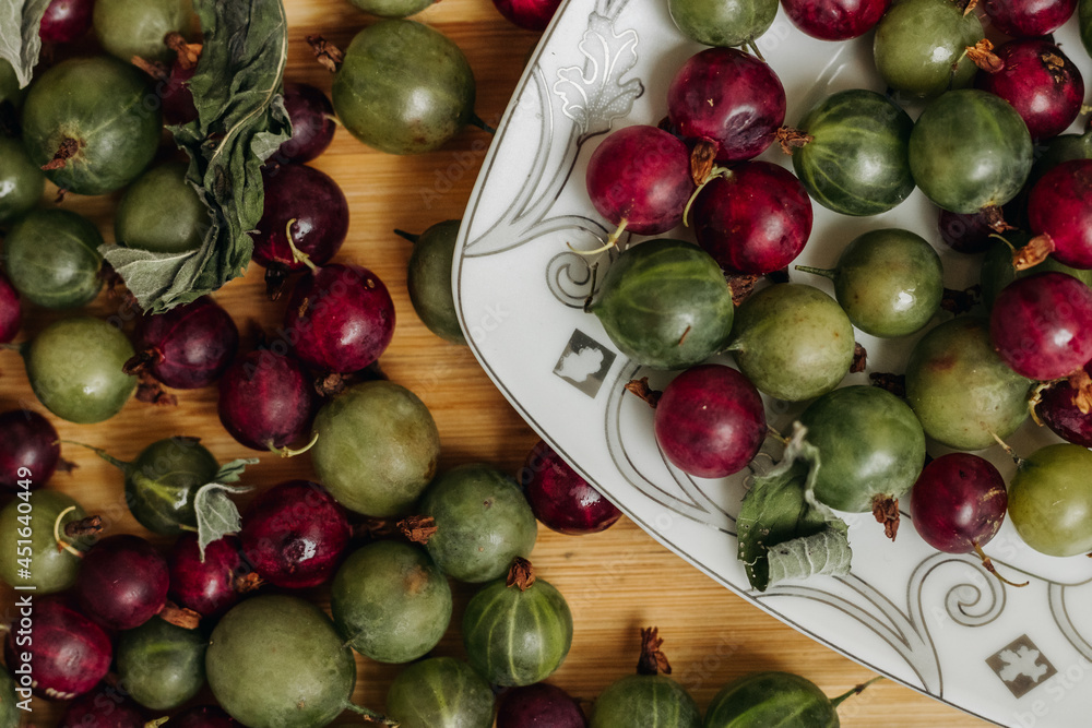 Green and red gooseberries. Gooseberries on a wooden surface and on a white plate. Plate with gooseberries Green and red gooseberries. Gooseberries on a wooden surface and on a white plate. Plate with gooseberries