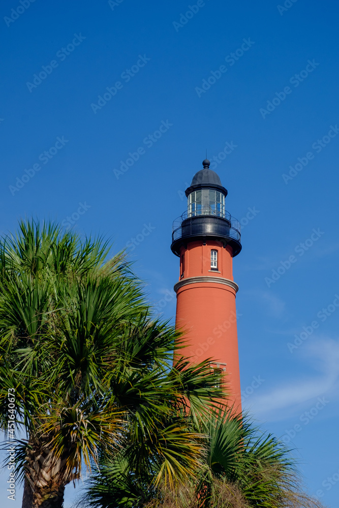 Vertical image of the tallest lighthouse in Florida and second tallest in the United States surrounded by palm trees in late afternoon light