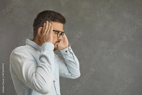 Tired young man in glasses eyes closed massaging temples trying to calm down, relieve stress, ignore everyday pressure at work and restore emotional balance standing isolated on copy space background