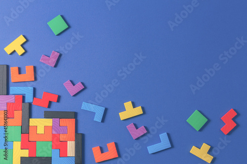 Different colorful shapes wooden puzzle blocks on blue background. Geometric shapes in different colors, top view, copy space