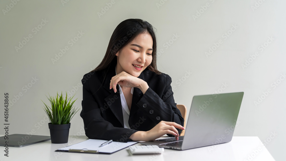 Image of happy smiling Asian businesswoman working on her laptop at the office. Image of happy smiling Asian businesswoman working on her laptop at the office.