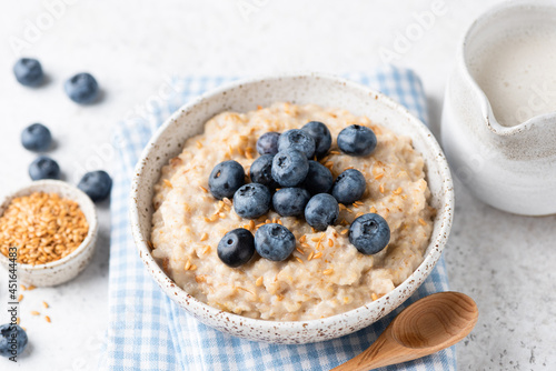 Vegan oatmeal porridge with blueberries and flax seeds in bowl on grey concrete background. Clean eating, dieting, weight loss concept