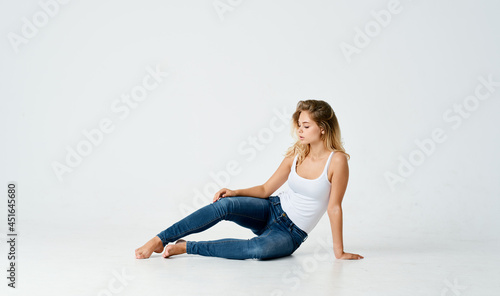 woman in white t-shirt and jeans sits on the floor light background studio model