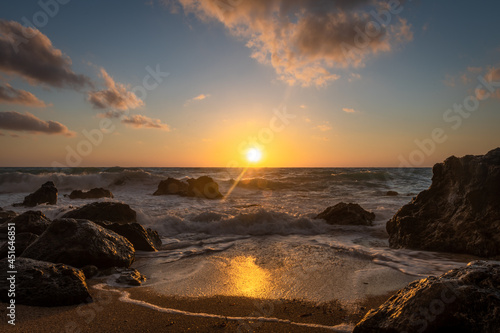 A beautiful golden sunset with reflections on the waves washing over the beach and the sun setting behind the horizon.