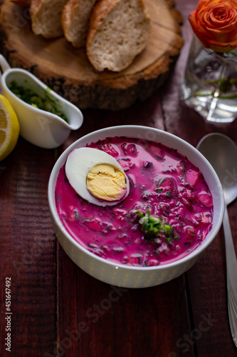 Cold borsch, summer beet soup with fresh cucumber boiled egg in a white bowl, bread, lemon. Traditional European food, delicious lunch
