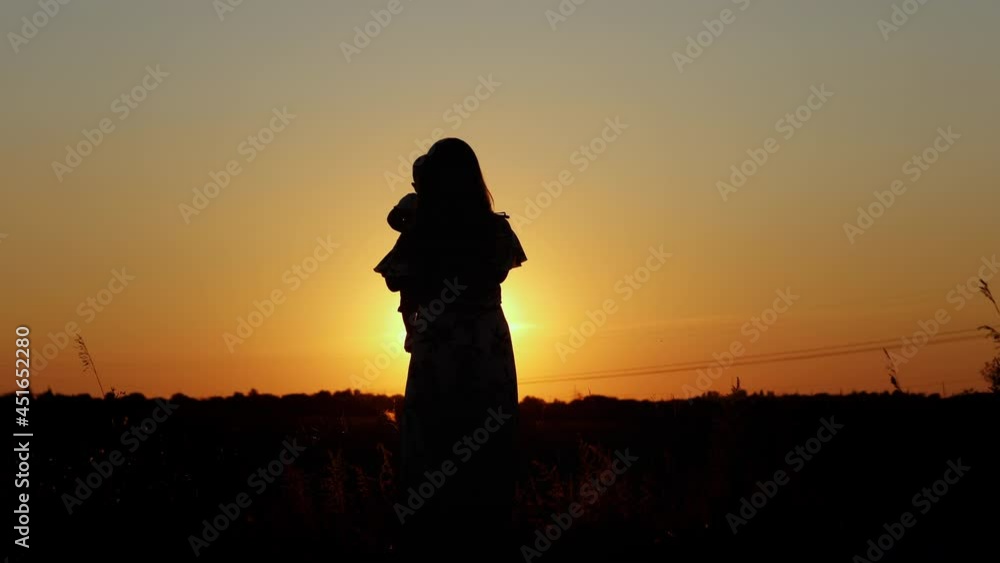 Unrecognizable silhouette at sunset, happy mother whirl her baby, hugs and kisses, motherly love Unrecognizable silhouette at sunset, happy mother whirl her baby, hugs and kisses, motherly love