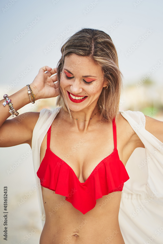 Cheerful woman on beach touching her hair and smiling