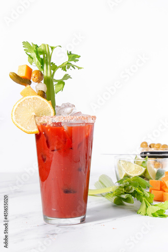 Bloody mary cocktail with celery, cheese, pickles, onions, and citrus on a white background