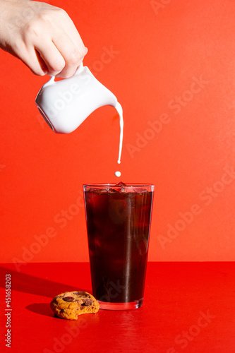 Iced coffee on a bright red background with a hand pouring cream into the coffee