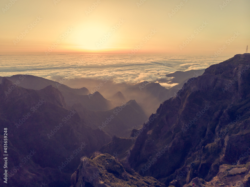 Spectacular landscape view of sunrise rising above sea of clouds surrounded with volcanic mountains.
