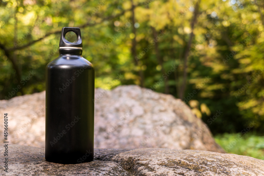 Black steel flask for water on a stone in the forest. The concept of a healthy lifestyle and care for the environment, avoiding the use of plastic. Black steel flask for water on a stone in the forest. The concept of a healthy lifestyle and care for the environment, avoiding the use of plastic.