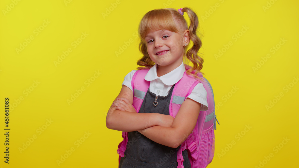 Attractive blond teenage student girl kid in school uniform wears pink backpack holding crossed arms, looking at camera, smiling isolated on yellow studio background. Education, back to school, study Attractive blond teenage student girl kid in school uniform wears pink backpack holding crossed arms, looking at camera, smiling isolated on yellow studio background. Education, back to school, study