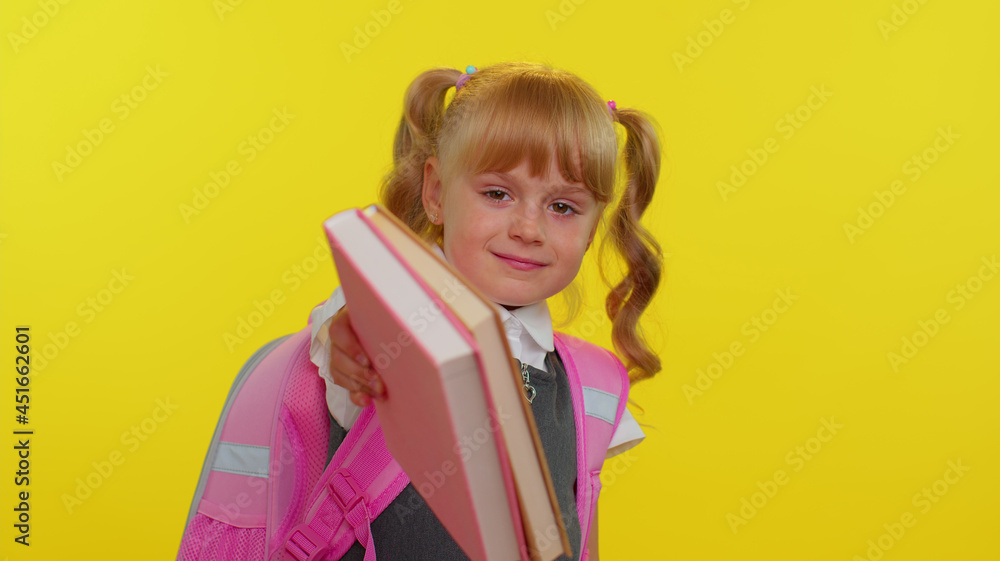 Happy pretty happy kid primary school girl with ponytails wearing uniform smiling grimacing looking at camera on yellow background. Little child student hugging books. Back to school concept Happy pretty happy kid primary school girl with ponytails wearing uniform smiling grimacing looking at camera on yellow background. Little child student hugging books. Back to school concept