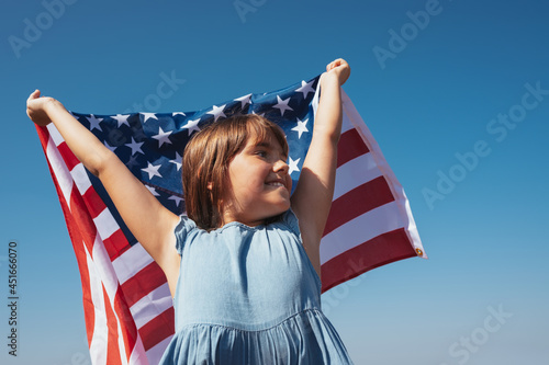 Portrait of a happy girl with the American flag in her hands against the background of the sky