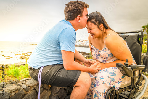 Disabled woman in wheelchair holding hand of her boyfriend while dating outdoors photo