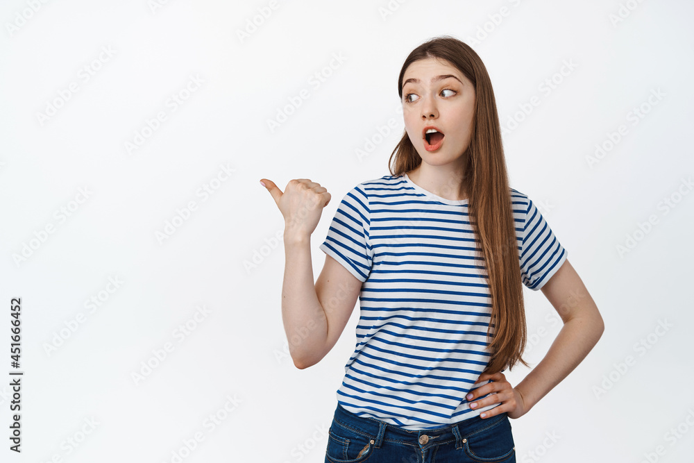 Portrait of woman say wow, pointing and looking left with surprised face, showing sale advertisement, standing over white background Portrait of woman say wow, pointing and looking left with surprised face, showing sale advertisement, standing over white background