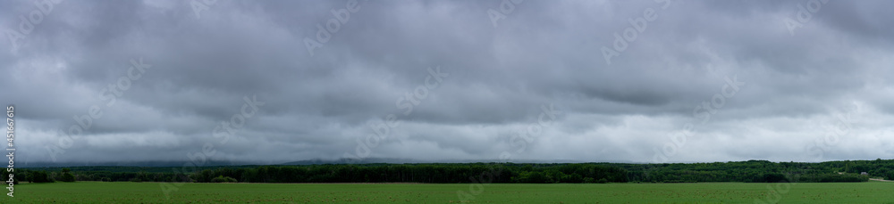 Panorama of a agriculture setting with a green field, trees in the midground and grey-blue clouds.
Panorama of a agriculture setting with a green field, trees in the midground and grey-blue clouds.