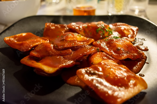 Traditional Italian ravioli filled with ricotta cheese, served with tomato sauce and basil leaves on a black plate. Close up.
