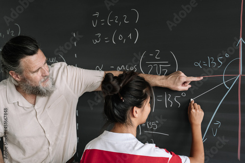 Asian Teenager Student doing Maths Exercises on Blackboard with teacher help in High School