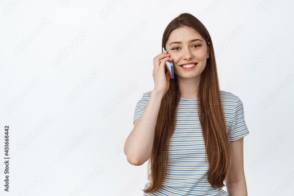 Cellular and mobile concept. Young woman talking on phone, making a call and smiling happy, standing against white background Cellular and mobile concept. Young woman talking on phone, making a call and smiling happy, standing against white background