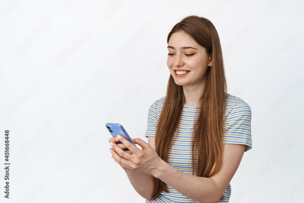 Cellular technology concept. Smiling young woman looking at mobile phone sceen with satisfied face expression, white background Cellular technology concept. Smiling young woman looking at mobile phone sceen with satisfied face expression, white background