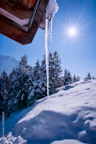 Gefrorener Eiszapfen auf dem Dach einer Berghütte in Contre-jour im Gegenlicht einer verschneiten Winteralm im Wettersteingebirge an einem sonnigen Tag - Postkartenmotiv  © HLPhoto
