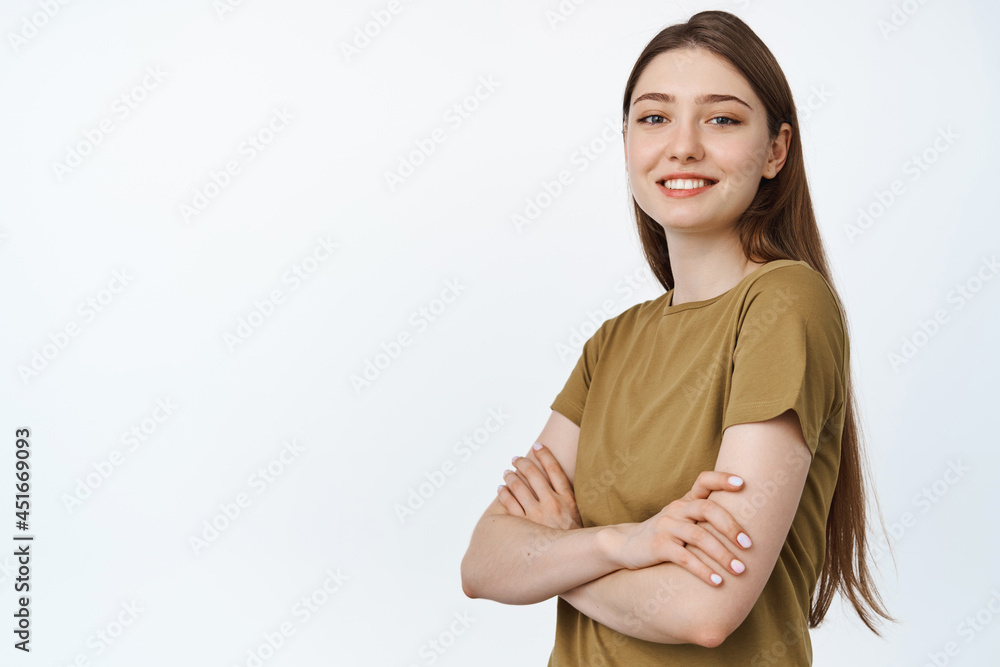 Obraz premium Young professionals. Smiling girl cross arms on chest and looking confident at camera, standing in tshirt against white background