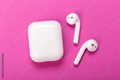 Modern wireless bluetooth headphones with charging case on pink background. The concept of modern technology.