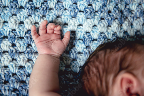 Infant child with single arm raised up above head while sleeping on blue knit background