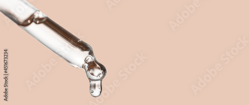 Cosmetics dropper, falling drop close up. Closeup of cosmetic pipette with essential oil dropping, serum with peptides on beige background. Self care concept. Beauty skin care product. Banner photo