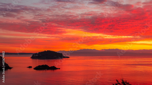 A vibrant red yellow orange sunset over the ocean waters with the Cascade Mountains in the distance in the Puget Sound of Washington state