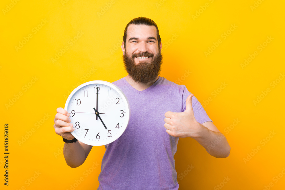 Happy bearded man is holding a round clock and showing thumb up. Happy bearded man is holding a round clock and showing thumb up.