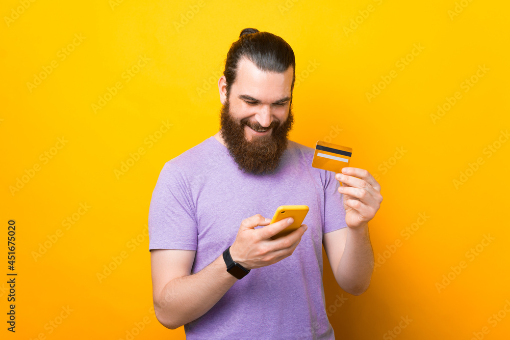 Joyful man is holding his phone and credit card, making some purchases online or using mobile banking. Joyful man is holding his phone and credit card, making some purchases online or using mobile banking.