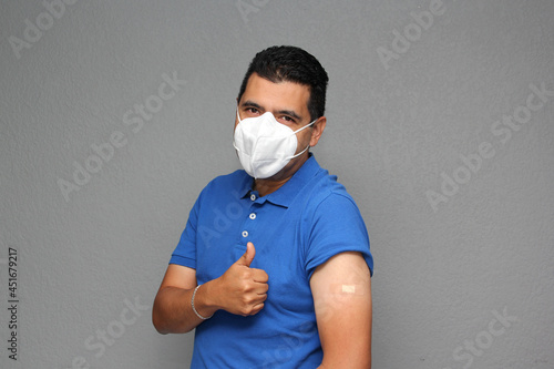 Happy Latino adult man shows his arm that just received the Covid-19 vaccine and has an adhesive band in the new normal of the pandemic
